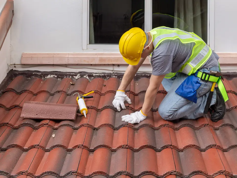 Roofer kneeling on a red tiled roof during a repair