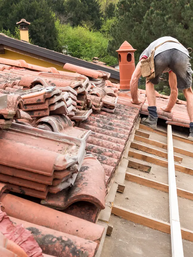 Roofer laying clay roof tiles on battens
